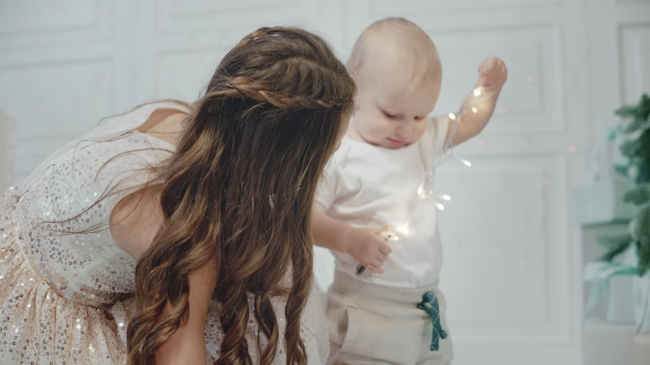 милый мальчик играет с гирляндой в гостиной. красивая сестра заботится о маленьком брате