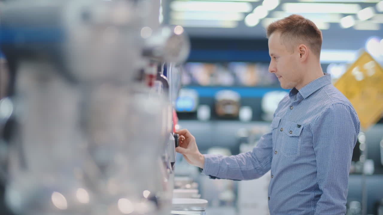 In the appliances store, the kitchen technician chooses the blender in his hands and considers the design and characteristics.