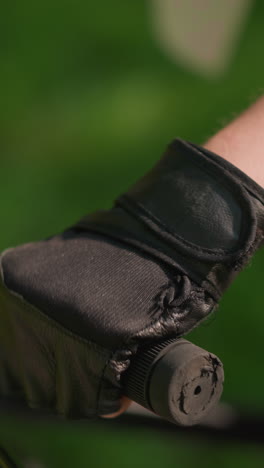 primer plano del manillar individual de la bicicleta con la mano en guante, el acelerador y el freno en uso, la luz solar se refleja suavemente en la mano con guante, con un fondo verde suavemente borroso
