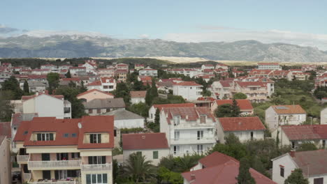 Antenne:-Flug-über-Türkisblaues-Meer,-Land-In-Novalja,-Kroatien-Natur-Mit-Häusern-Und-Blauem-Himmel-Und-Sonne