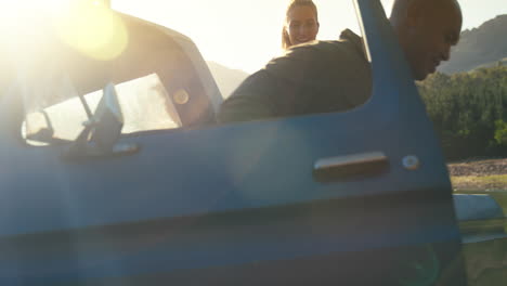 Group-Of-Friends-Unloading-Backpacks-From-Pick-Up-Truck-On-Road-Trip-By-Lake-In-Countryside