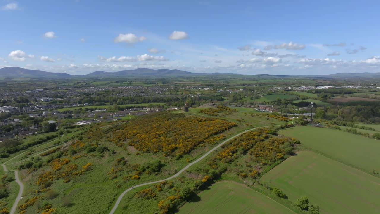 Vinegar Hill, Enniscorthy, County Wexford, Ireland, April 2025. Drone panoramic aerial establishing pullback gradually reveals hiking paths through low scrub vegetation and nearby town buildings.