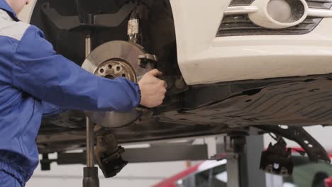 mecánico de automóviles reemplazando las patas de freno de la rueda del automóvil levantado en la estación de servicio de reparación
