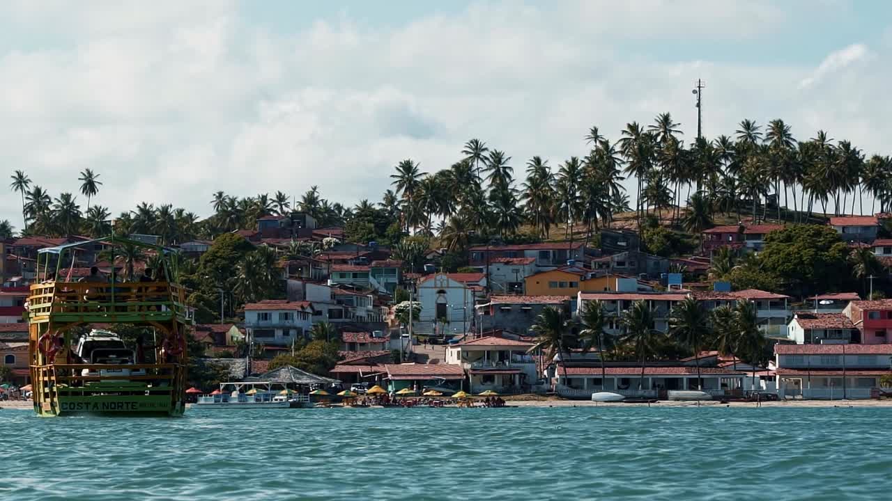 incline hacia abajo la toma en cámara lenta de un barco de transporte que navega hacia la ciudad costera tropical de barra do cunhaú en rio grande do norte, brasil desde la playa de restinga tropical en un día soleado de verano