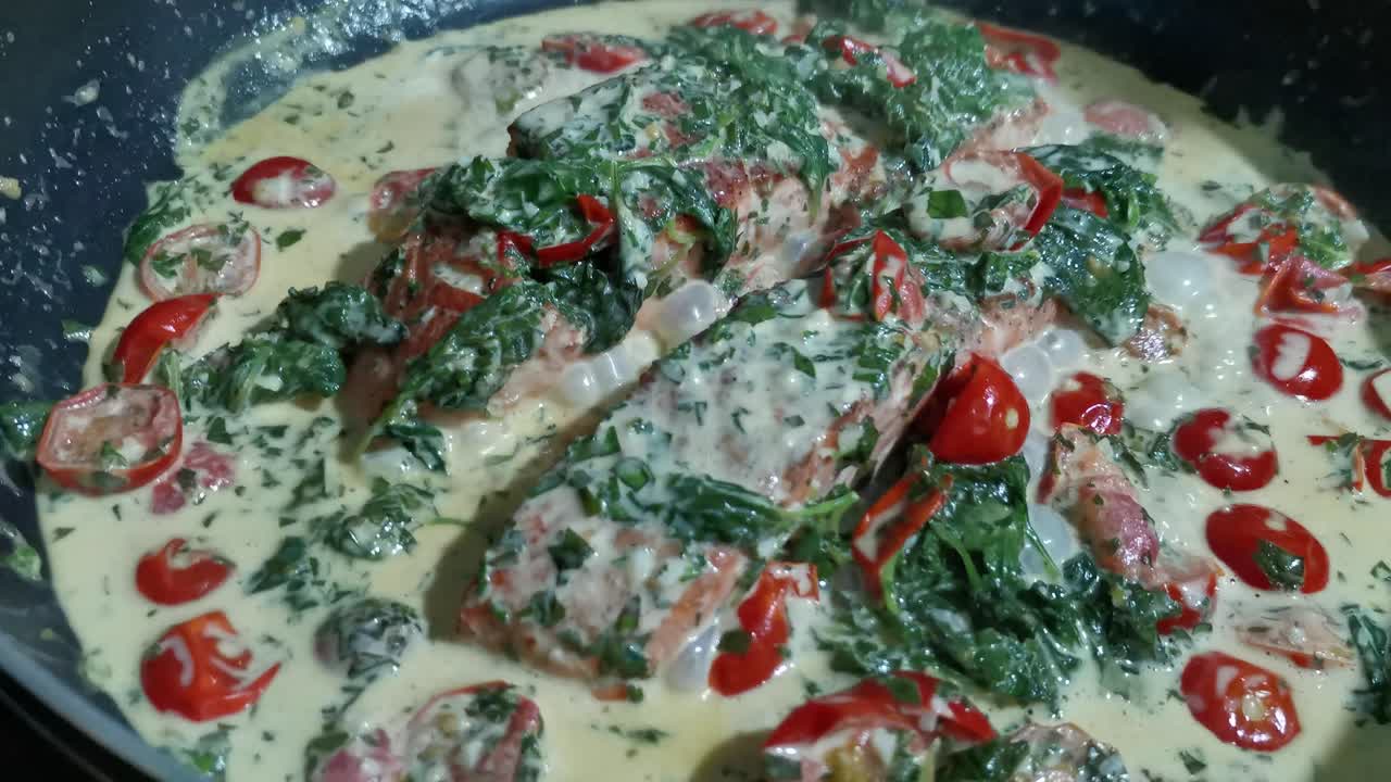 Salmone scottato in padella con spinaci cremosi e pomodori, cotti lentamente in padella a fuoco medio, sobbollendo dolcemente