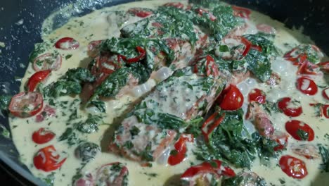 salmone cotto in padella con spinaci cremosi e pomodori che si cucinano lentamente in una padella a fuoco medio, bollendo su un fuoco lento e bollente