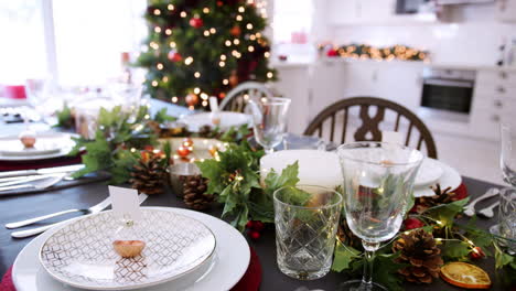 a close up, slow panning shot showing a festive christmas dining table with bauble name card holders arranged on plates and green and red seasonal decorations