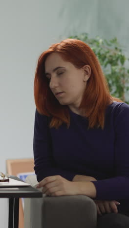 woman takes off glasses to let eyes rest after work on laptop from home. tired female redhead freelancer sits on sofa in evening looking at computer