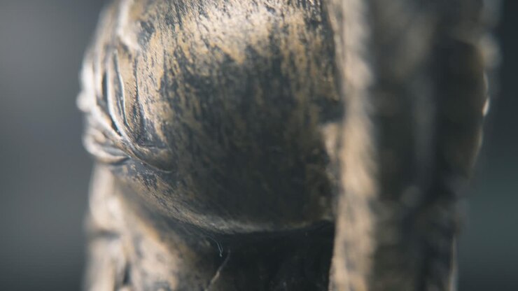 Una ripresa macro dettagliata in slow motion con movimento di tilt verso l'alto da dietro di un design di volto spartano, elmo da guerriero greco antico in bronzo, su un supporto rotante a 360 gradi, illuminazione da studio, movimento fluido in 4K