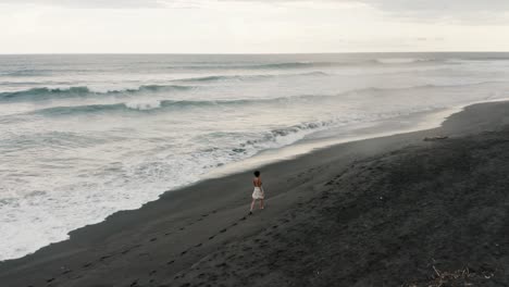 woman walking on the black sand beach of el paredon in guatemala - aerial drone shot