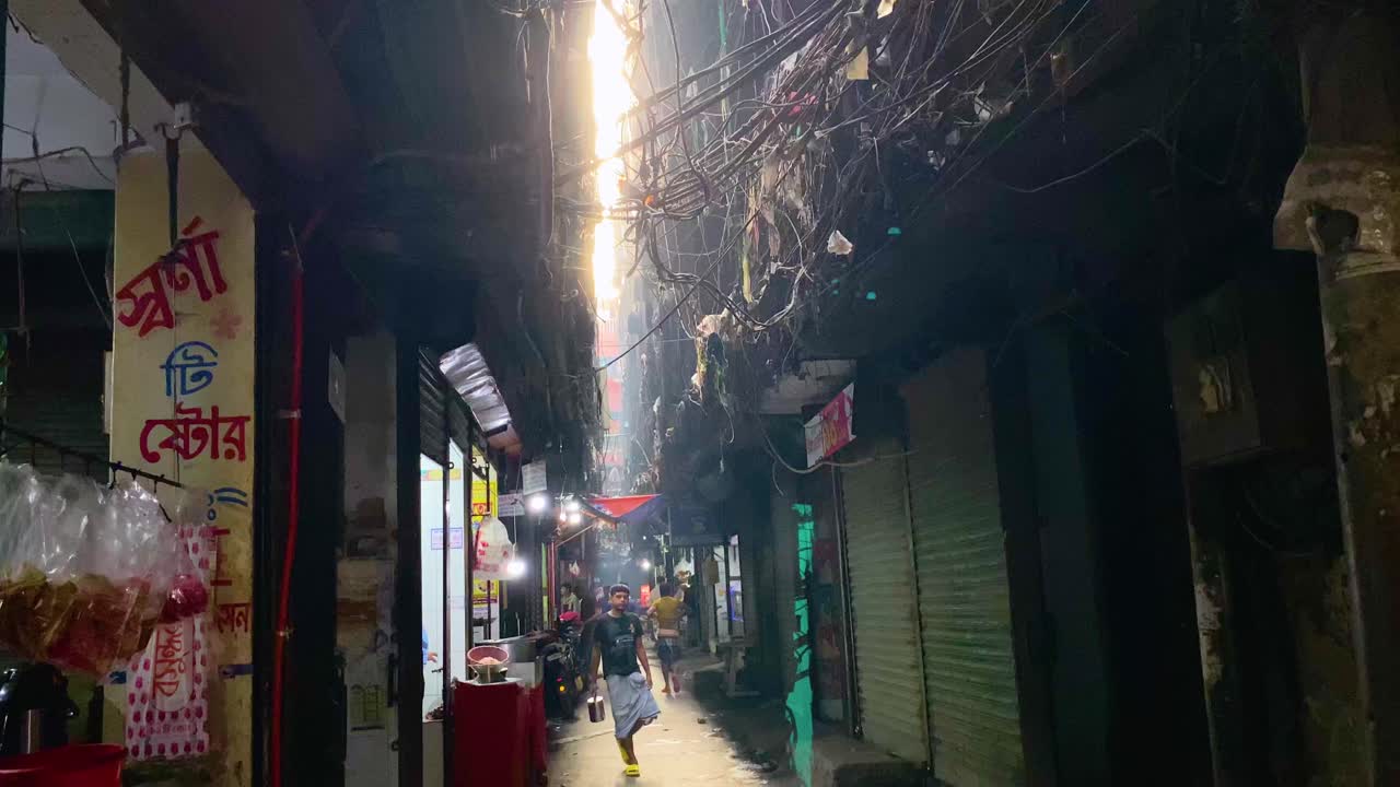 People Walking Along The Narrow Street With Tangled Power Lines In Old Dhaka, Bangladesh. - tilt down shot