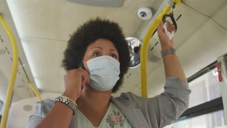 Plus-size-biracial-woman-wearing-face-mask-talking-on-smartphone-in-bus