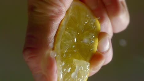 Person-Squeezes-Sliced-Lemon-Half-Splashing-Juice-Around