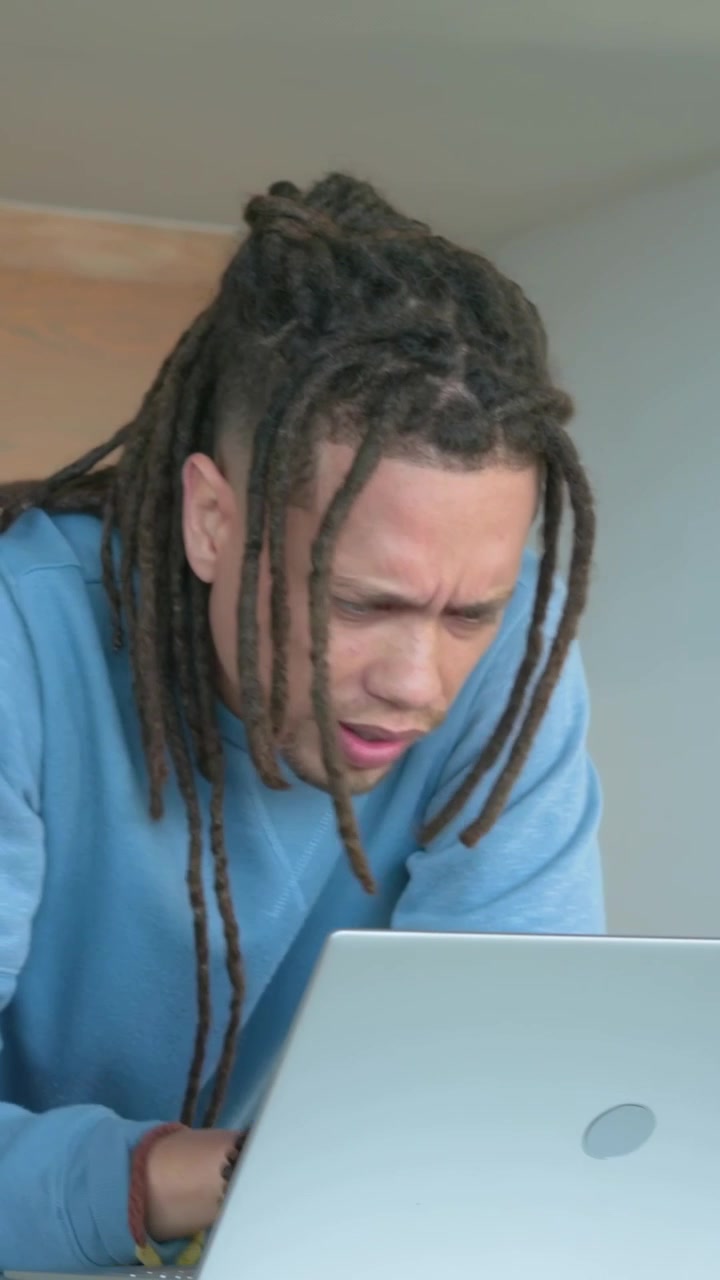 Vertical video: Reading laptop, man in sweater working using touchpad in kitchen, camera panning