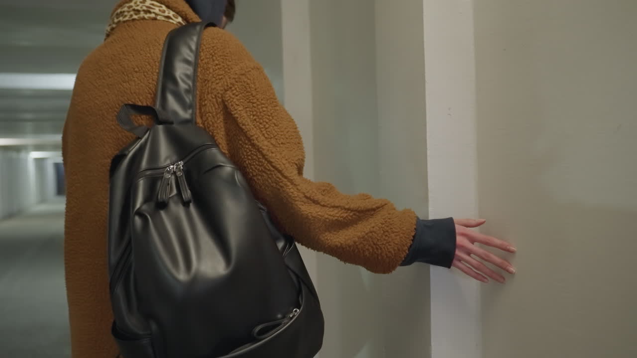A close-up shot of a girl wearing a brown coat and carrying a black backpack as she gently touches a wall with her hand. sense of contemplation and the tactile connection with the surroundings