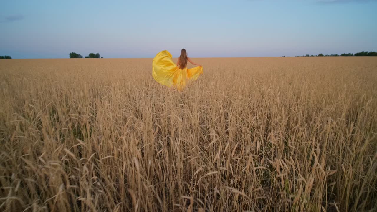 Woman in Yellow Dress Walking Through a Golden Wheat Field at Sunset