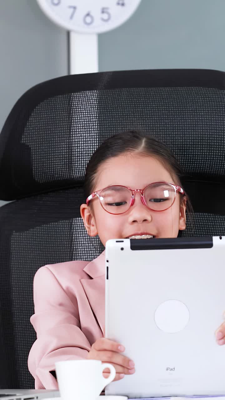 Una bambina vestita da donna d'affari usa un tablet mentre è seduta in un ufficio.
