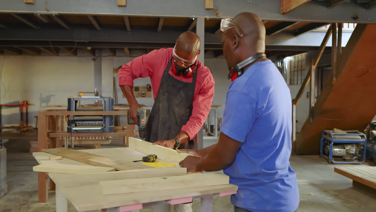 Positioning planks African American coworkers drilling pilot holes explaining technique in workshop