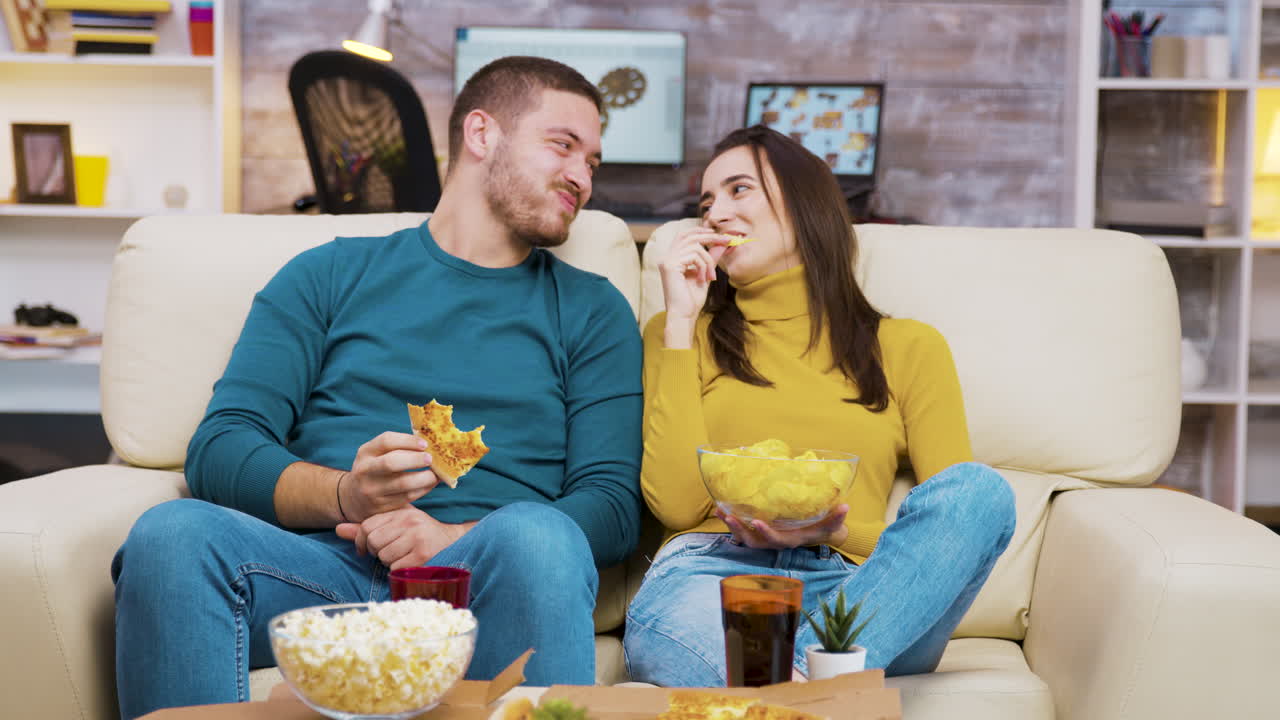 Coppia che mangia pizza e snack sul divano