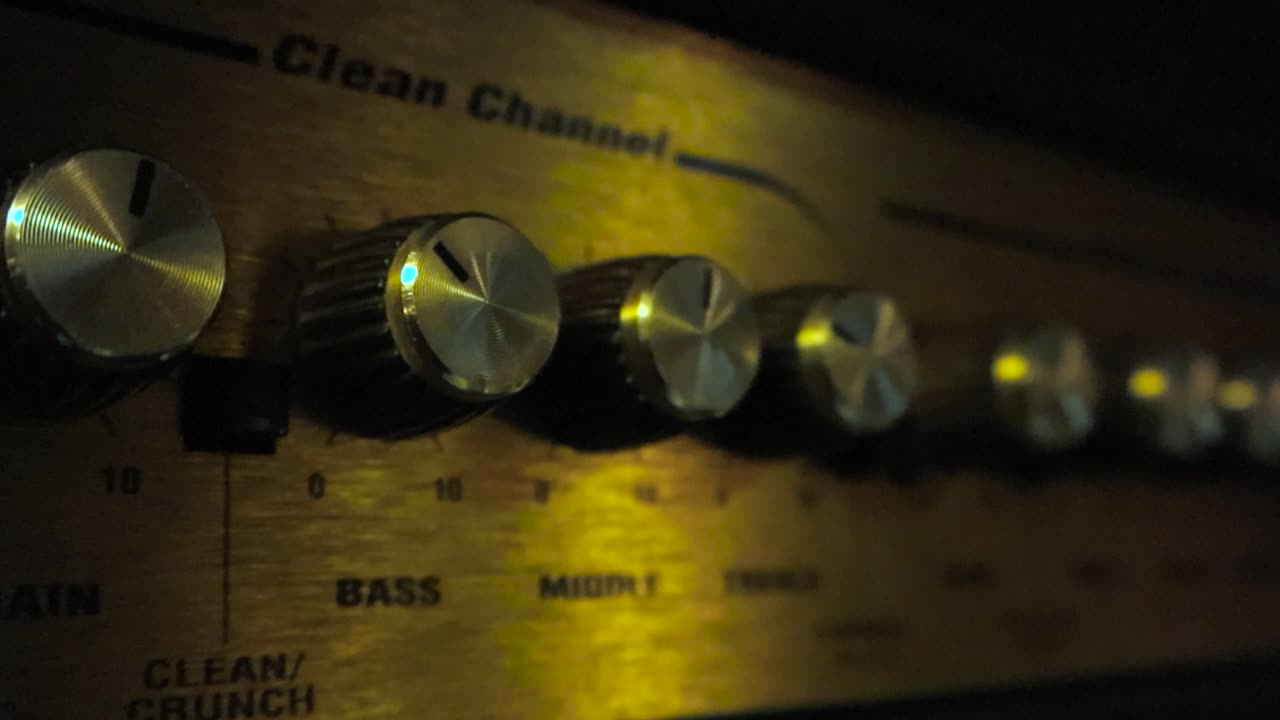 Close up or close up footage of Left to right cinematic panning of a golden shiny and reflective guitar amp or amplifier knobs and buttons at a studio room that have indicator lines on them.
