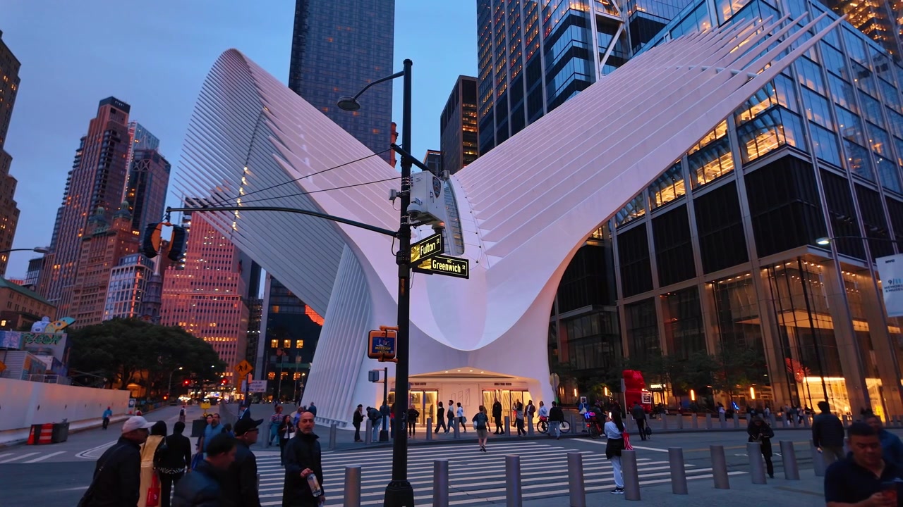 New York, USA, 5 giugno 2026: Pedoni all'Oculus, Lower Manhattan, New York. Attraversamento pedonale, segnali stradali e ali bianche a coste si ergono sotto torri di uffici in vetro al crepuscolo blu.