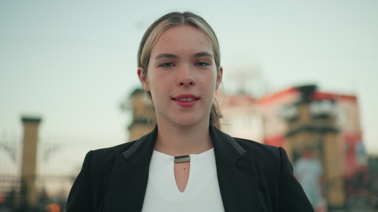 Close up of white lady standing confidently outdoors in modern setting, hands on waist, exuding calm and assurance with blurred view of people walking in background