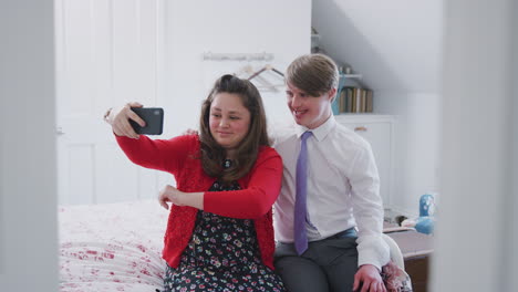 pareja de jóvenes con síndrome de down sentados en la cama usando el teléfono móvil para tomarse una selfie en casa