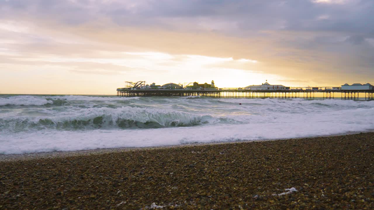 Slow Motion Waves Crashing on Brighton Beach with Palace Pier in Background with Sunset Back Lighting with Dynamic Colorful Cloudscape