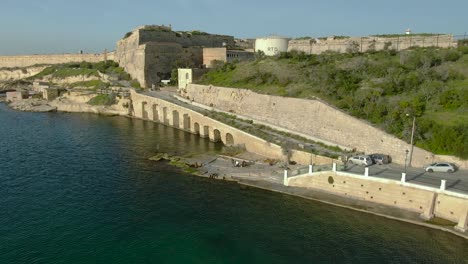 Dronie-Aerial-Shot-over-the-sea-away-from-a-crane-and-an-old-city-and-a-fort