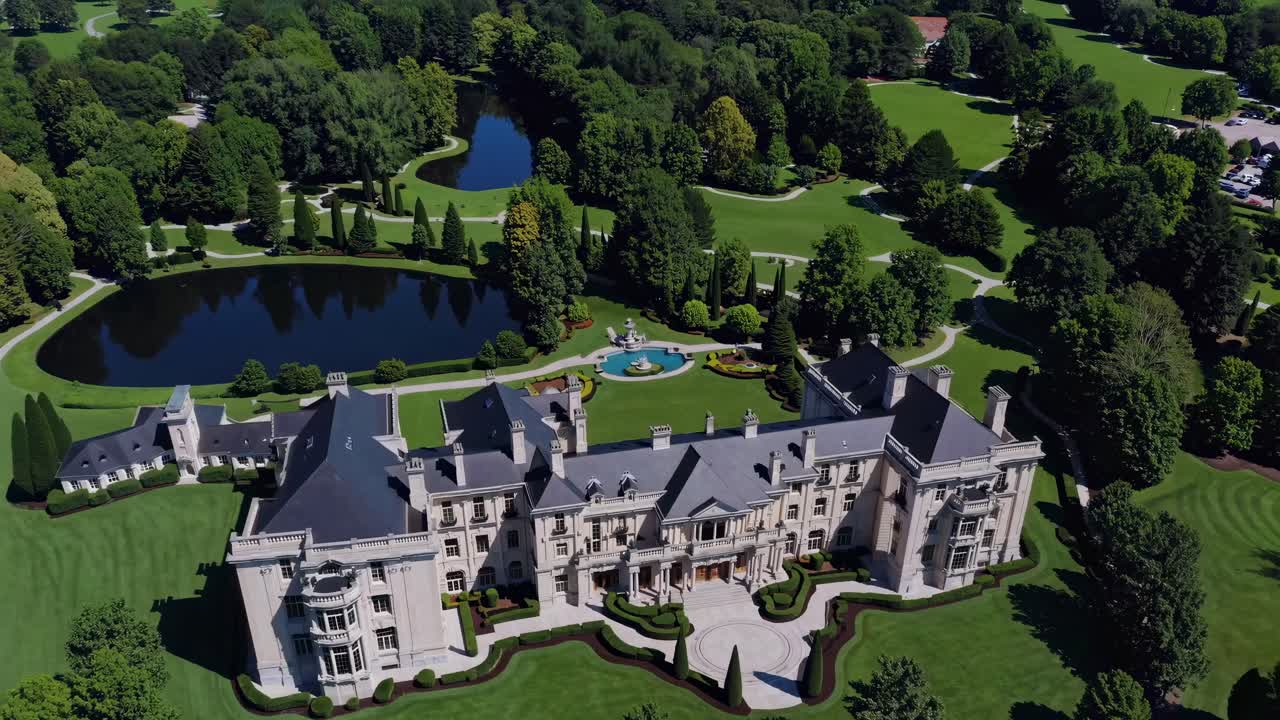 Aerial view of an elegant mansion surrounded by lush greenery and tranquil water features, showcasing the grandeur and beauty of luxurious estate living in a serene environment