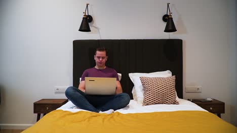 a young man opens the laptop, is using the laptop in his bedroom, browsing on the internet, typing something with a keyboard