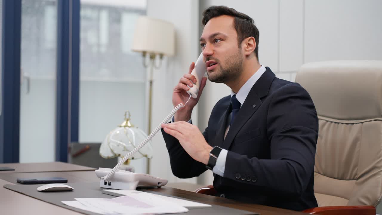 Stress at work. A nervous angry businessman talking on the phone sitting at the office, man is deeply disappointed with bad news or reports issues