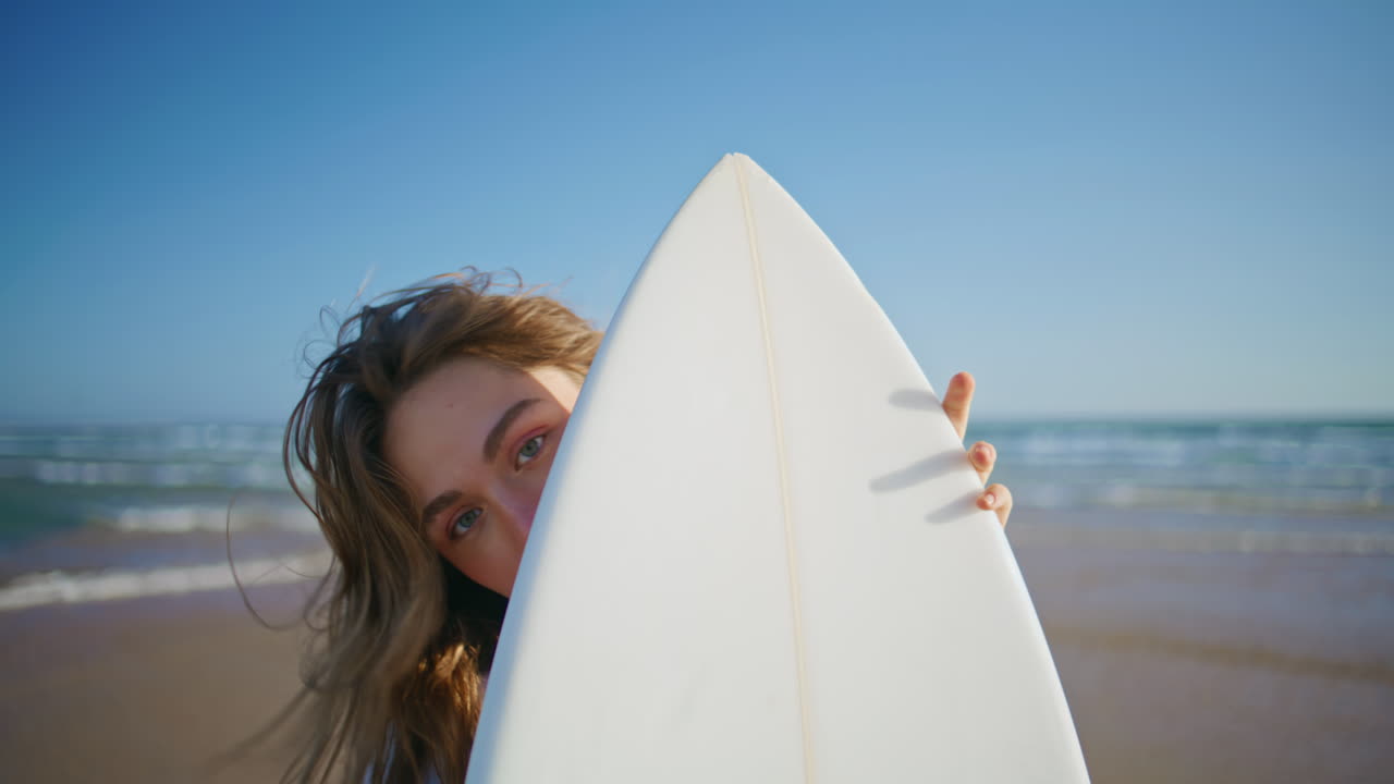 Søt jente kikker på surfebrett og tilbringer tid på stranden, nærbilde. Kvinne med vind i håret