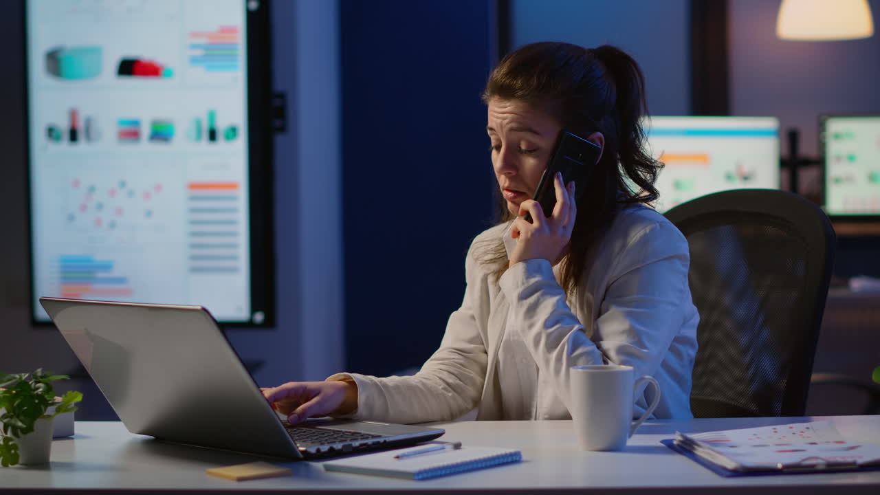 Kvinnelig ansatt snakker i telefon mens hun jobber på laptop