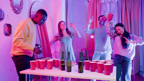 happy multiethnic young friends dancing and having fiun during a beer pong party at home.