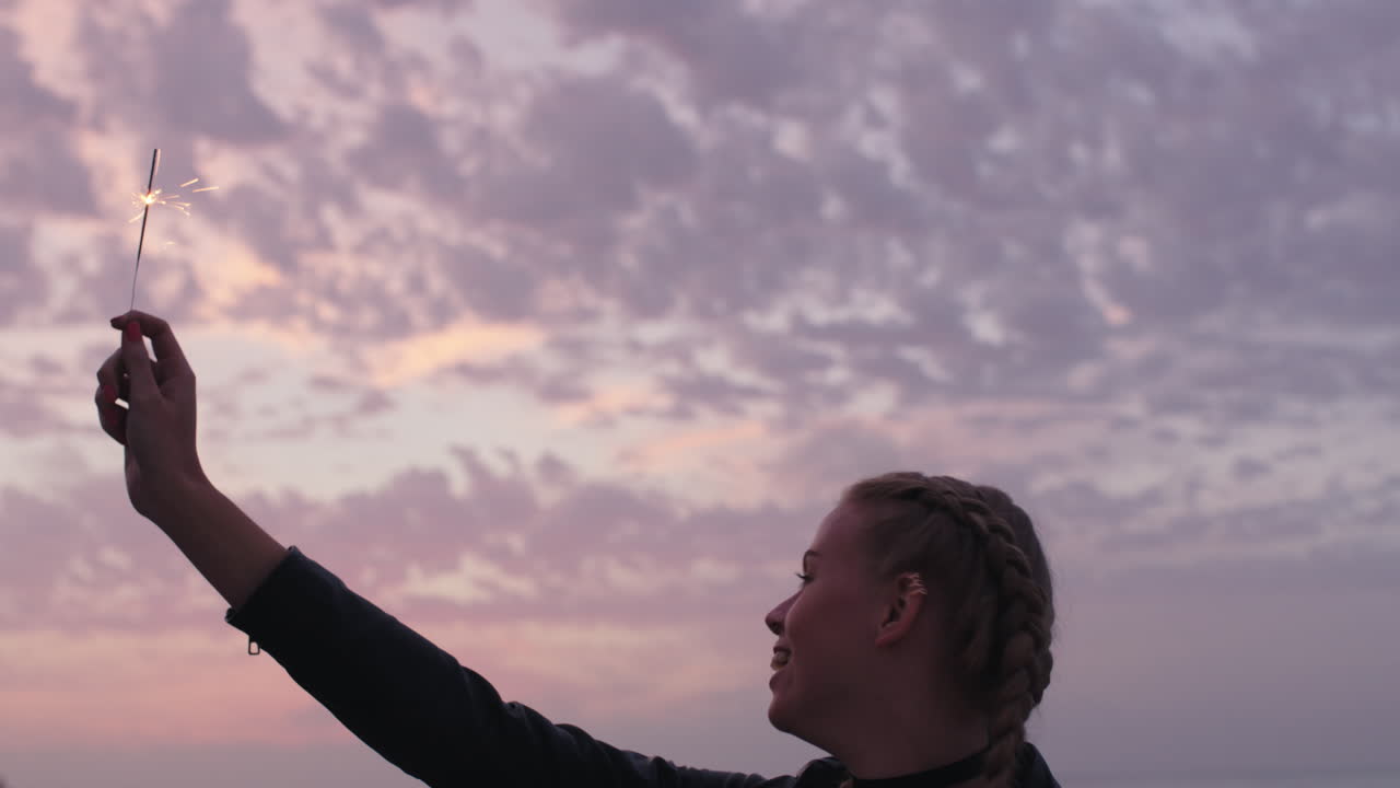 hermosa mujer rubia sosteniendo fuegos artificiales brazos levantados sonriendo celebrando en la playa