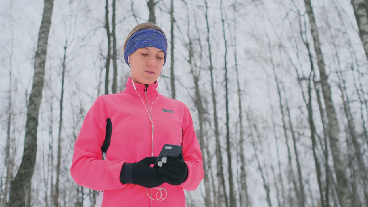 A young woman on the morning jog holds in her hands a smartphone picks a music track for training. Winter run. Use modern gadgets and training applications