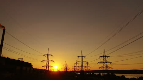 sunset among high voltage towers. transmission lines on the setting sun background. electricity distribution in the evening. motion camera back.