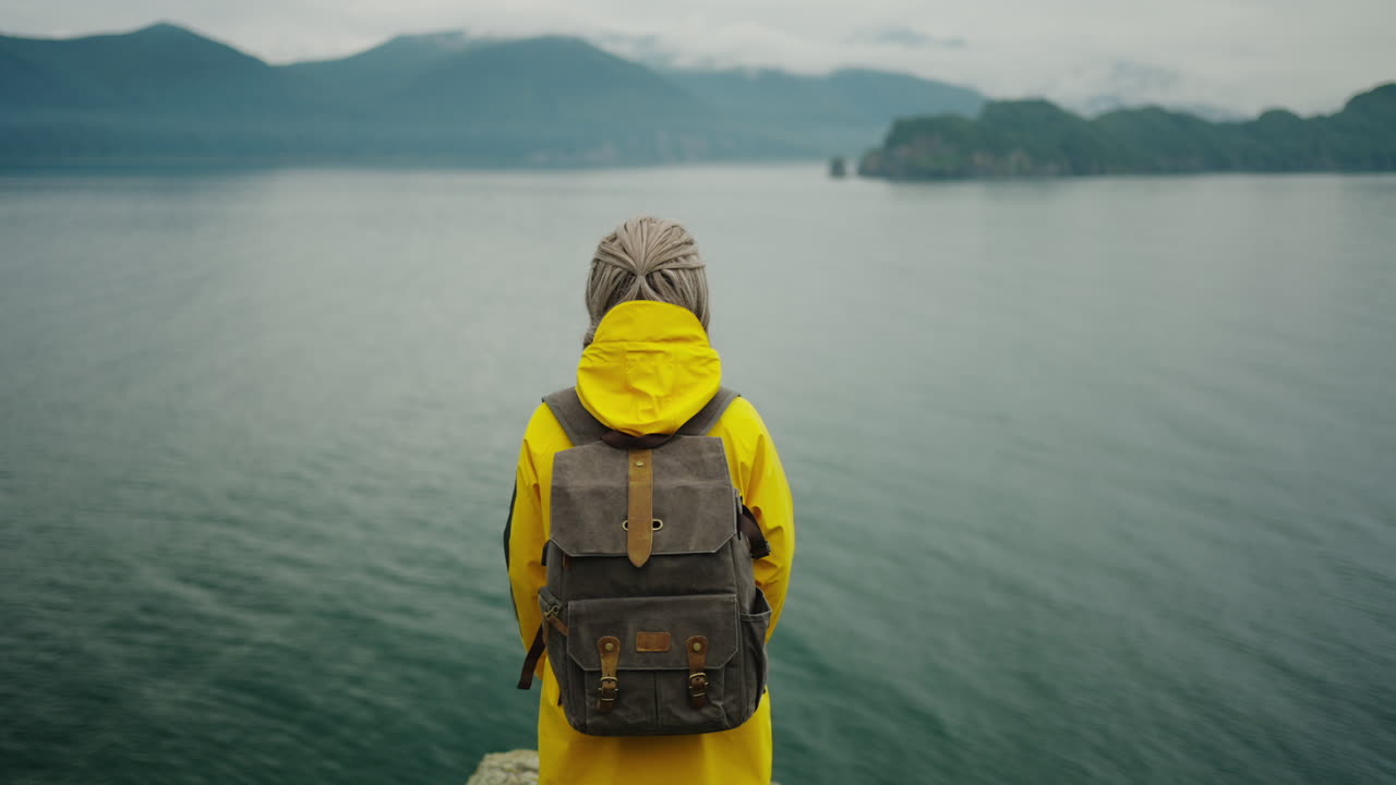 Donna che fa escursioni con un impermeabile giallo, vista panoramica del paesaggio