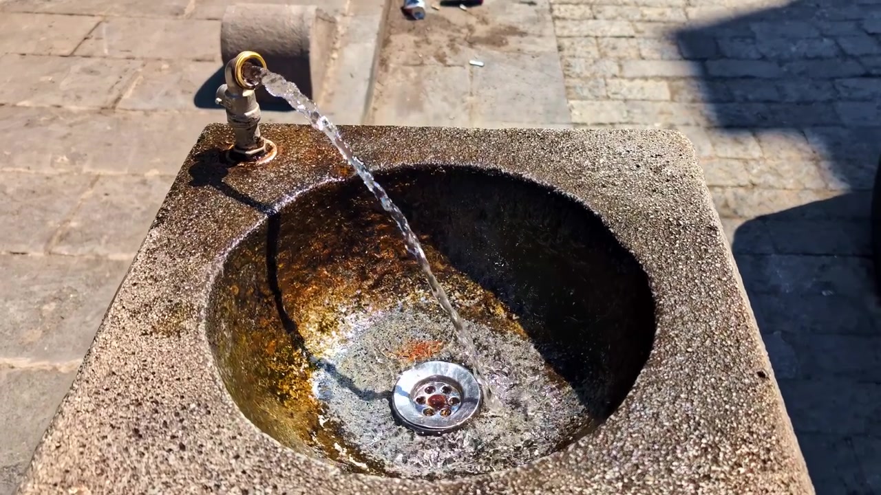 ティフリスの晴れた都会の通りにある公共の石造りの給水栓から水が流れ出る様子。