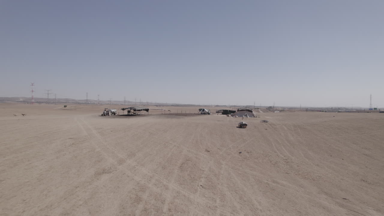 Bedouin residential tents without a permit in a remote and desert area, near a highway and large power poles, dry land without crops, push in shot