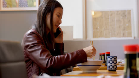 Woman-having-noodles-while-talking-on-mobile-phone-4k