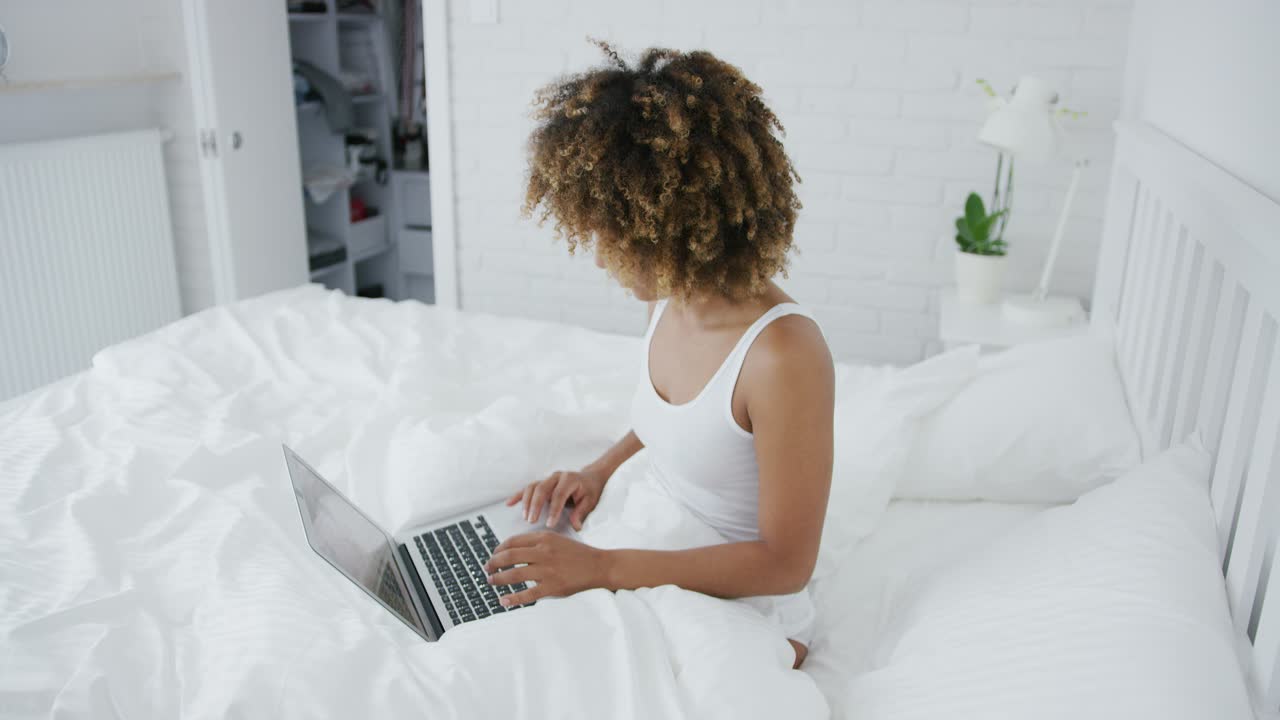Pretty woman lounging on bed with laptop