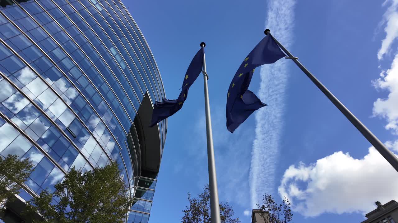 Bandiere dell'UE sventolano sotto un cielo blu accanto alla facciata in vetro curvato del Lex Building nel quartiere europeo di Bruxelles