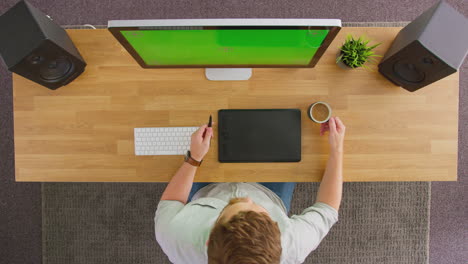 overhead view of male graphic designer or retoucher working at computer with green screen in office