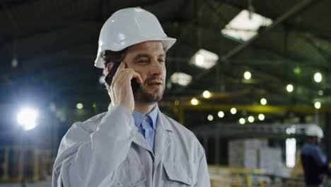 caucasian engineer wearing a helmet and talking on the phone in a factory