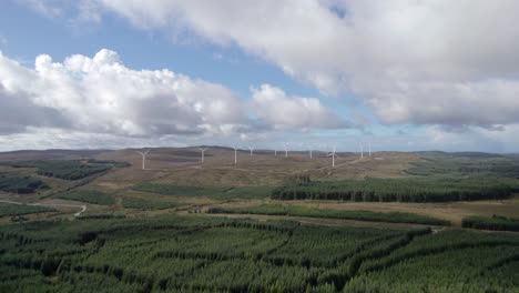 aerial drone footage of multiple turning wind turbines in a scottish windfarm surrounded by forestry plantations of commercial conifers on the kintyre peninsula, argyll, scotland