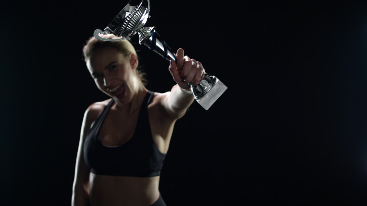 mujer emocionada sosteniendo en las manos la copa del campeón sobre un fondo negro. victoria deportiva