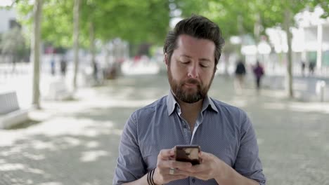 Bearded-man-messaging-via-smartphone-outdoor