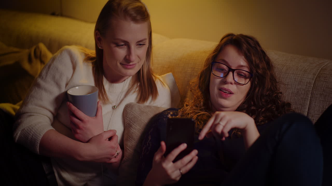 Two women relaxing on couch while watching a smartphone